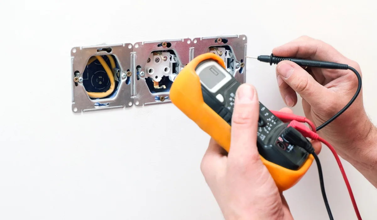 Electrical fault testing and inspection in Gauteng Electrician testing an electrical wall circuit with a multimeter during fault finding